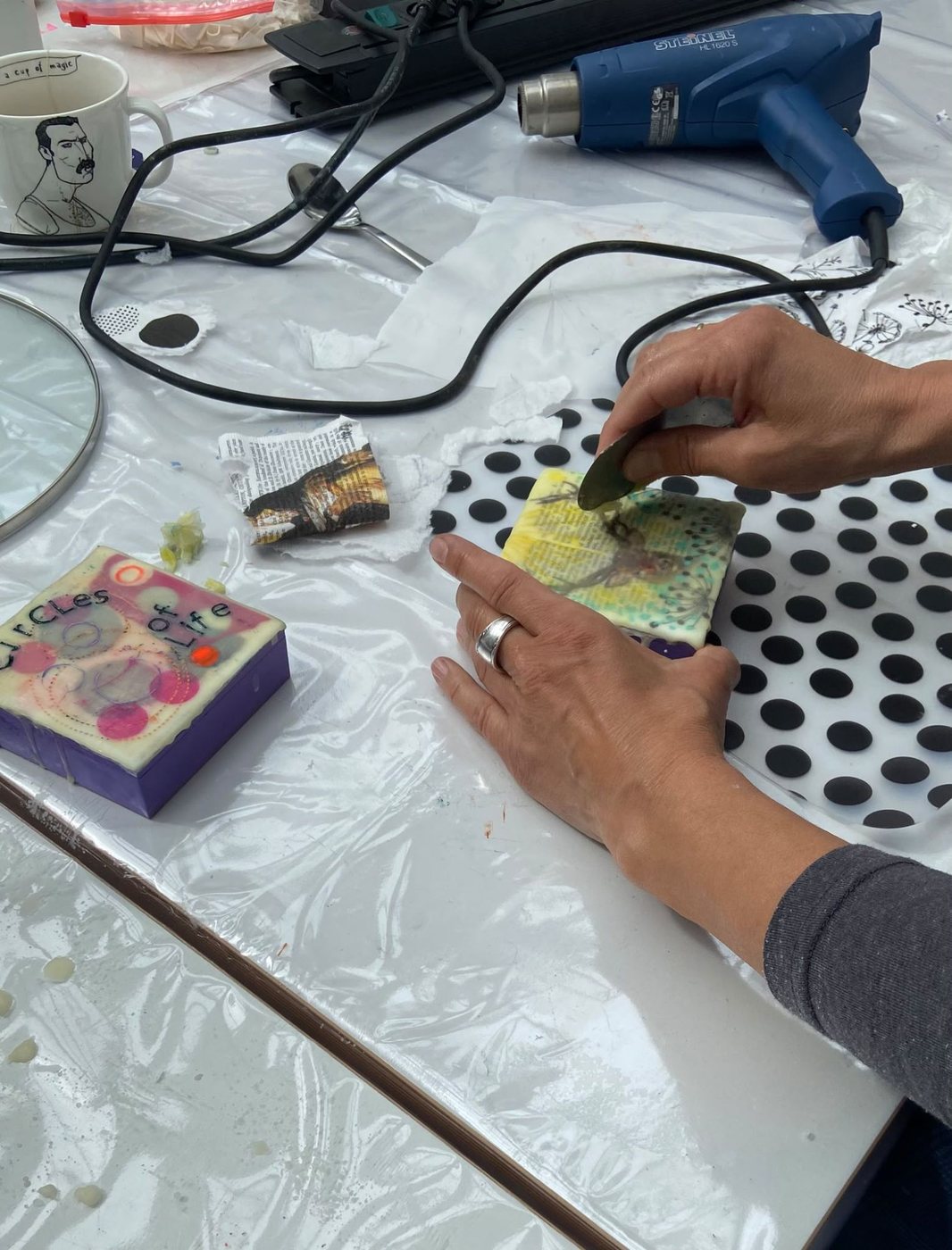 Im Workshop: Wachs wird mit dem Spachtel bearbeitet, daneben das fertige Bild „Circles of Life“